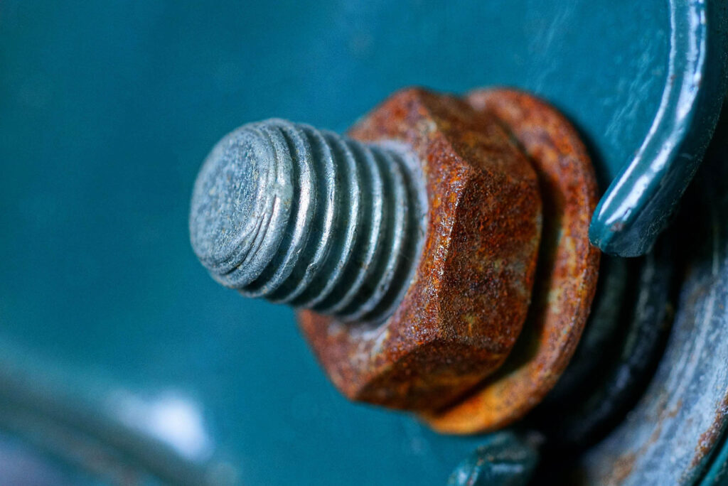 A gray bolt and rusty brown nut on a green metal wall