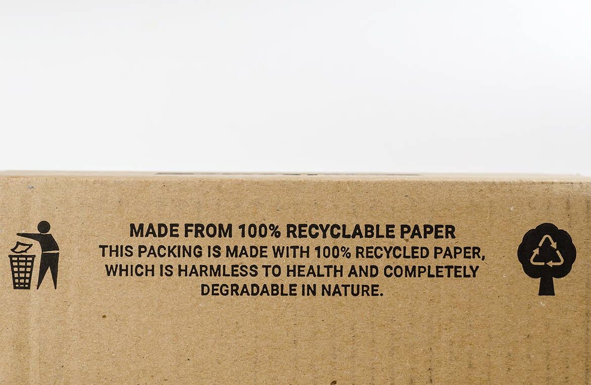 Recycled cardboard packaging with printed sustainability icons and a message stating it is made from 100% recyclable paper.